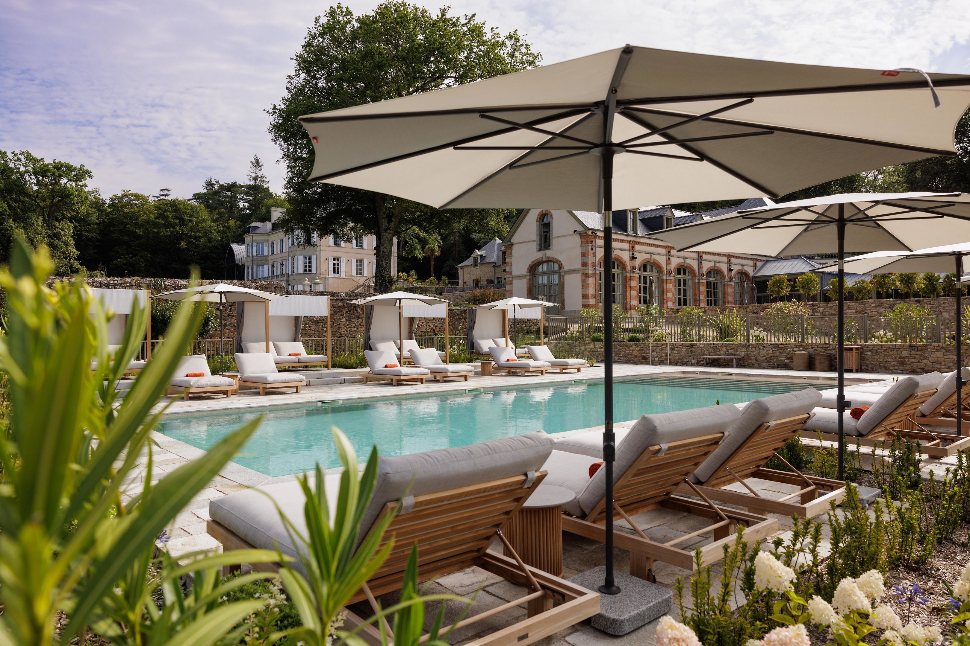 A poolside area with lounge chairs and umbrellas, surrounded by stone walls and greenery.