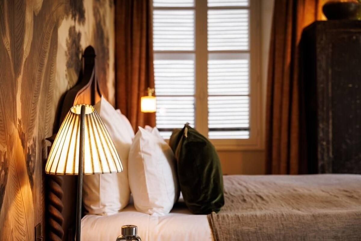 A hotel room with a bed, a lamp, and a window with curtains.