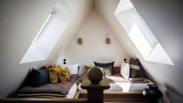 Un dormitorio cálido en el ático con techo inclinado, dos tragaluces, una cama con ropa de cama estampada y una mesita con una lámpara.