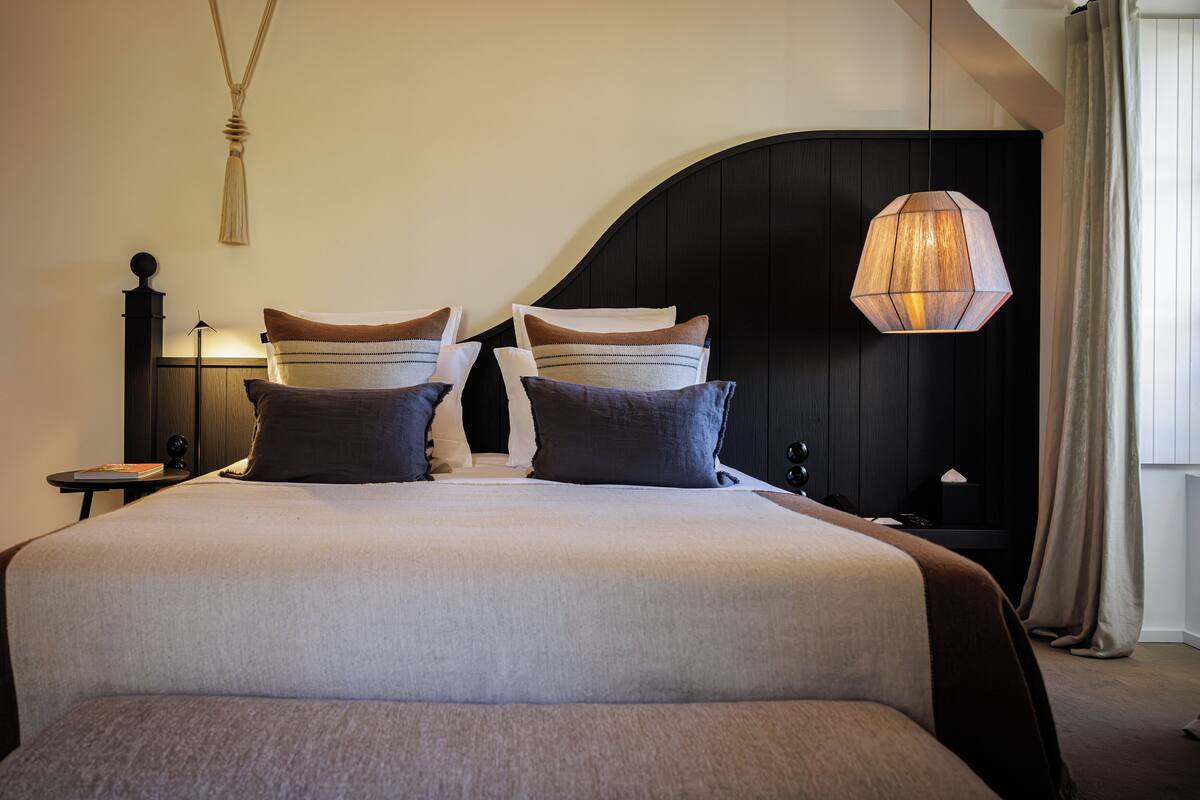 A neatly made bed with a large pillow and a bedside table with a lamp.