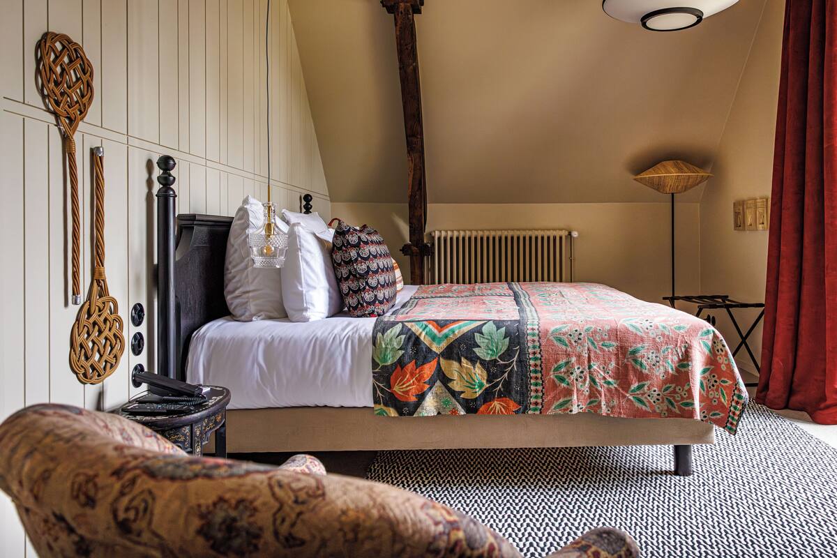A bedroom with a large bed, a wooden headboard, a radiator, a floor lamp, and a patterned throw blanket.