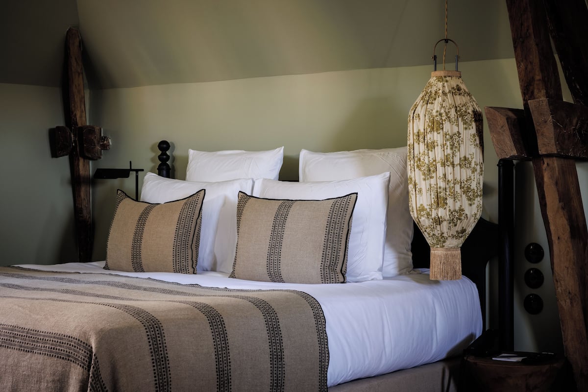 A neatly made bed with white and beige bedding, a hanging lantern, and wooden wall decor.