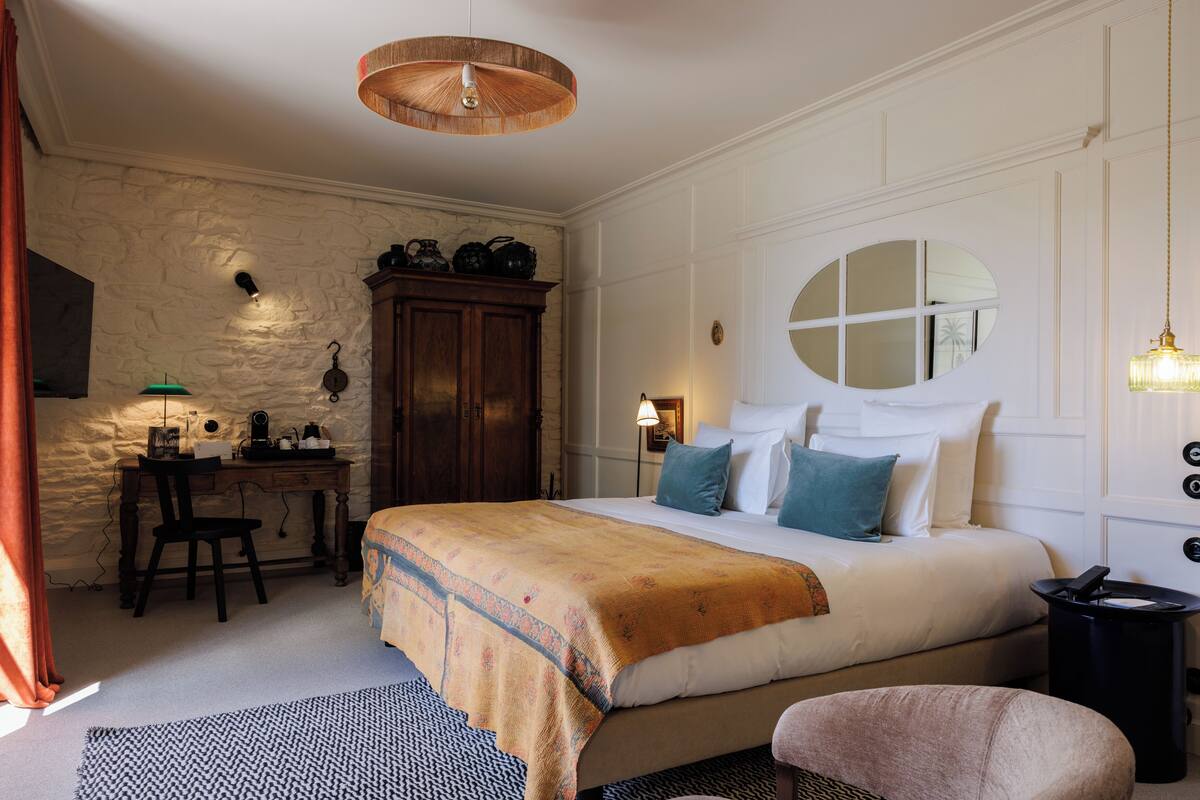 A bedroom with a large bed, a desk, a chair, and a round mirror on the wall.