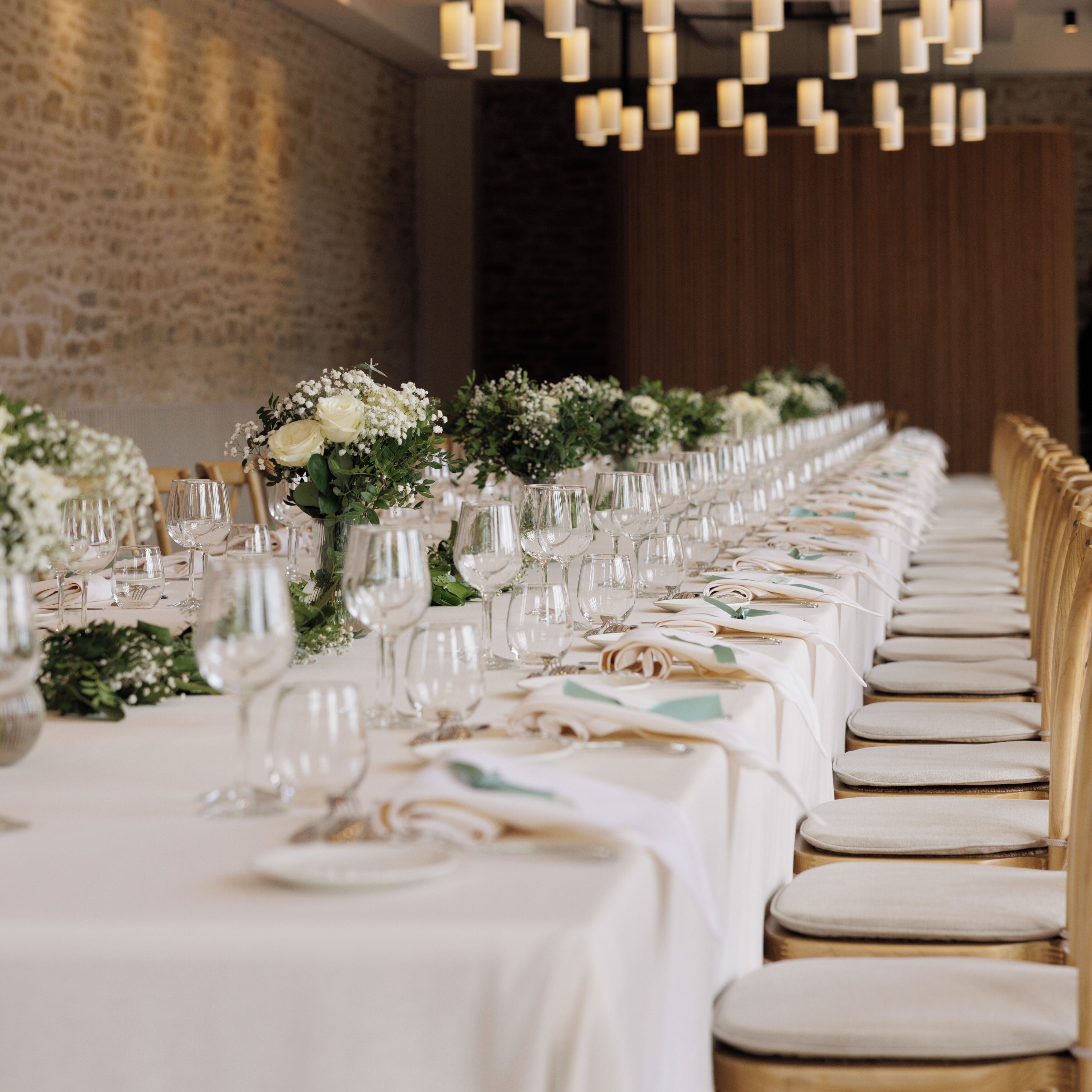 A long banquet table set with white tablecloths, glassware, and floral centerpieces.