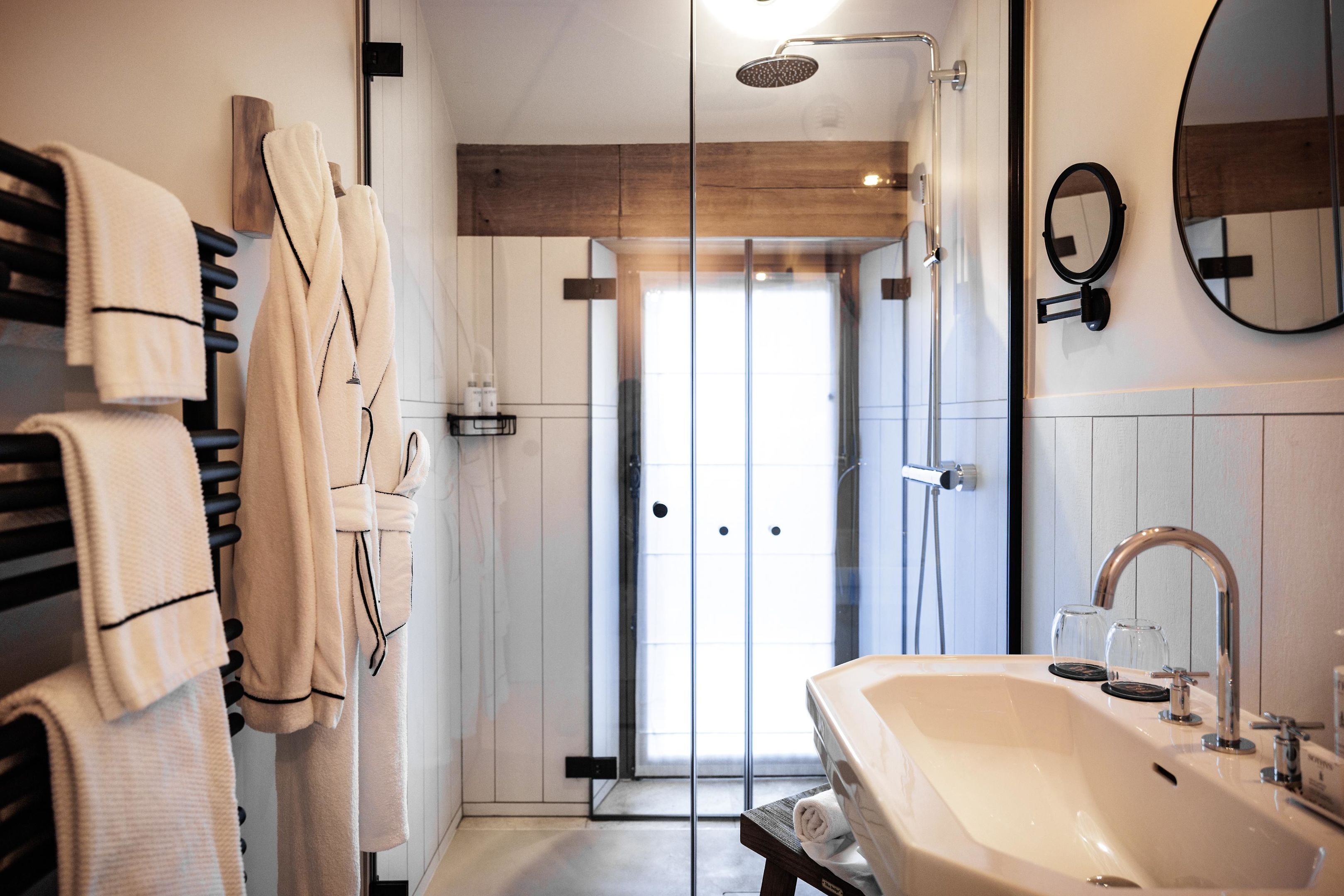 Een moderne badkamer met een groot wastafelmeubel, een douchecabine met glazen wanden en handdoeken aan een rek.