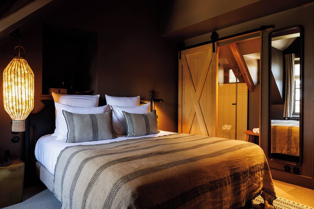 A bedroom with a large bed, a hanging light fixture, a wardrobe, and a mirror.