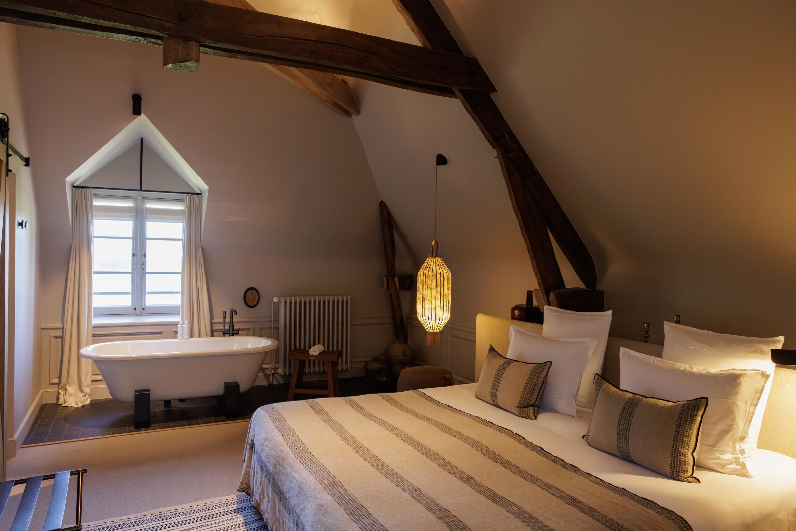 A bedroom with a large bed, a window, a bathtub, and a hanging light fixture.