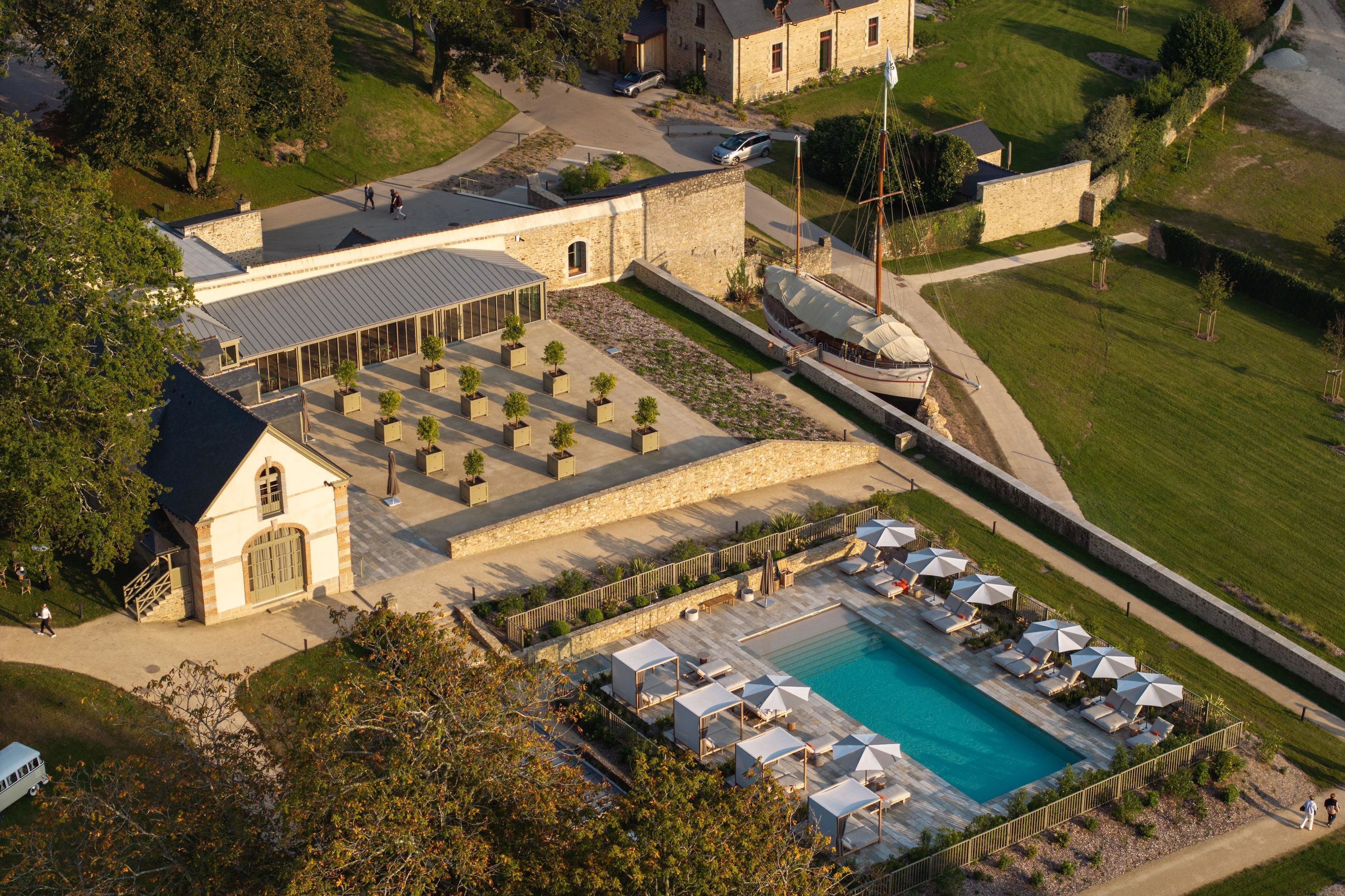 Luchtbeeld van een resort met een zwembad, buitenzitplaatsen en een historisch gebouw.