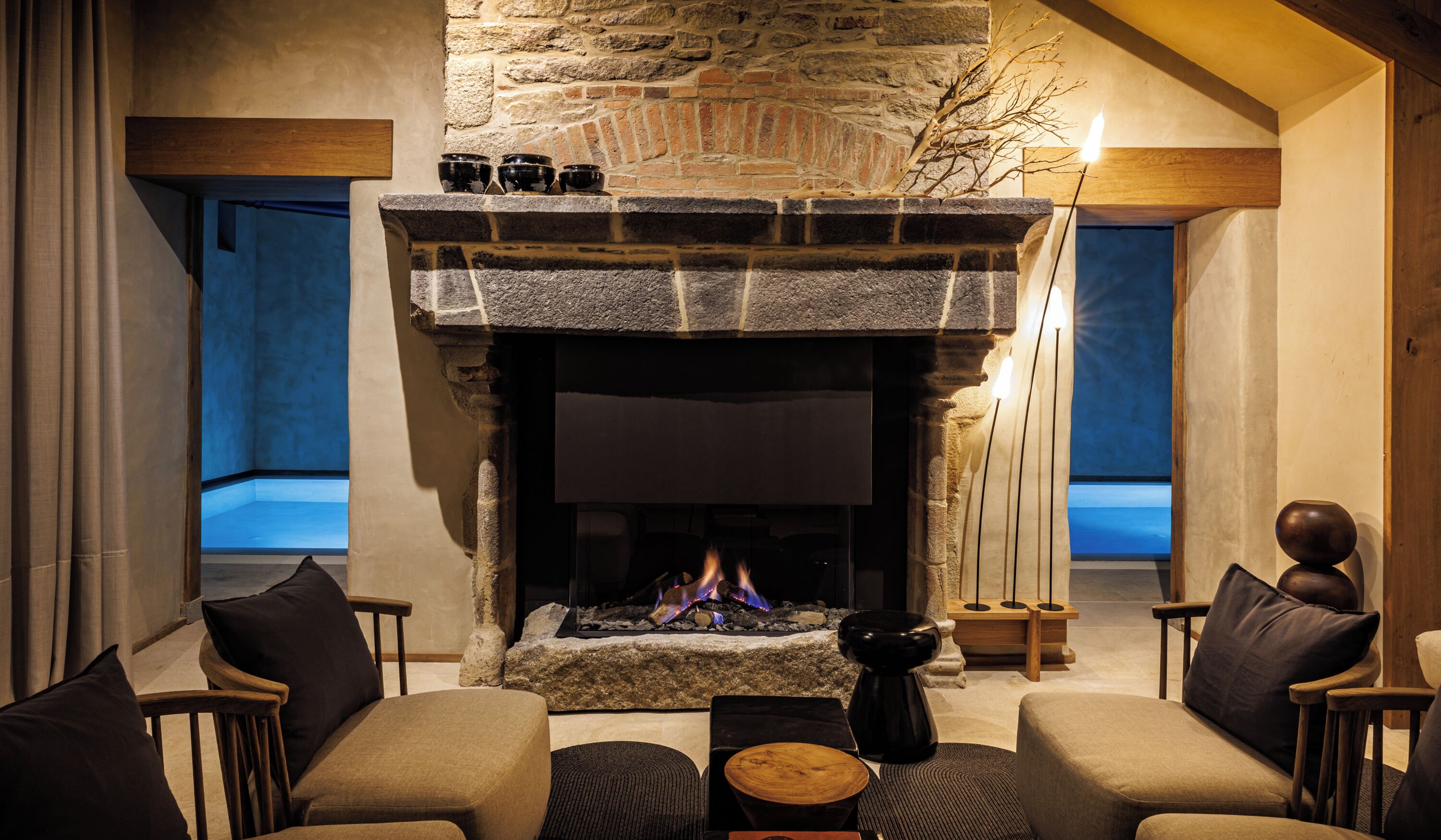 Un salon chaleureux avec une cheminée en pierre, des sièges confortables et une vue sur l’extérieur.