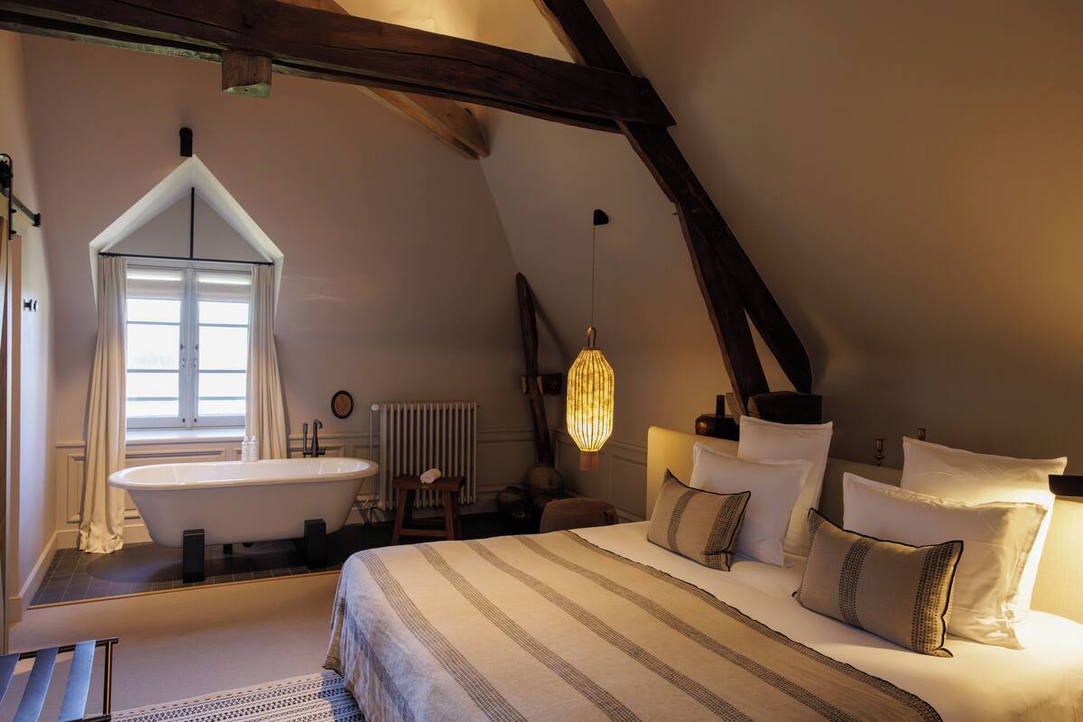 A bedroom with a large bed, a window, a bathtub, and a hanging light fixture.