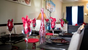 A dining table set with red and white vases, a ceiling fan, and artwork on the walls. - The Oasis (Portmore)