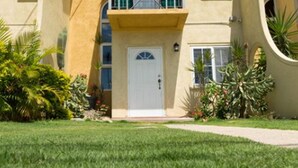 A two-story building with a central entrance, a balcony on the upper floor, and a small garden area in front. - The Oasis (Portmore)