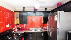 A modern kitchen with red and black cabinetry, stainless steel appliances, and a granite countertop. - The Oasis (Portmore)