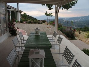 A covered outdoor seating area with a table and chairs, surrounded by greenery and flowers. - Ktima Noosfera wellness & retreat center (Xylokastro-Evrostina)