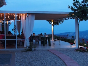 An outdoor patio with tables and chairs, a pergola with string lights, and a view of the mountains. - Ktima Noosfera wellness & retreat center (Xylokastro-Evrostina)