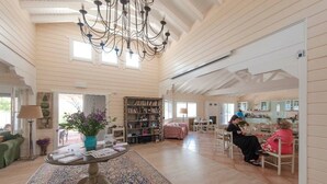 A spacious living room with a large chandelier, a bookshelf, and a dining area with chairs. - Ktima Noosfera wellness & retreat center (Xylokastro-Evrostina)