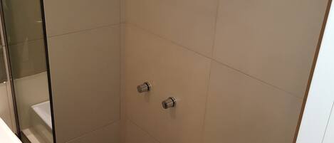 Un baño pequeño y moderno con cabina de ducha de vidrio, inodoro blanco y lavamanos.