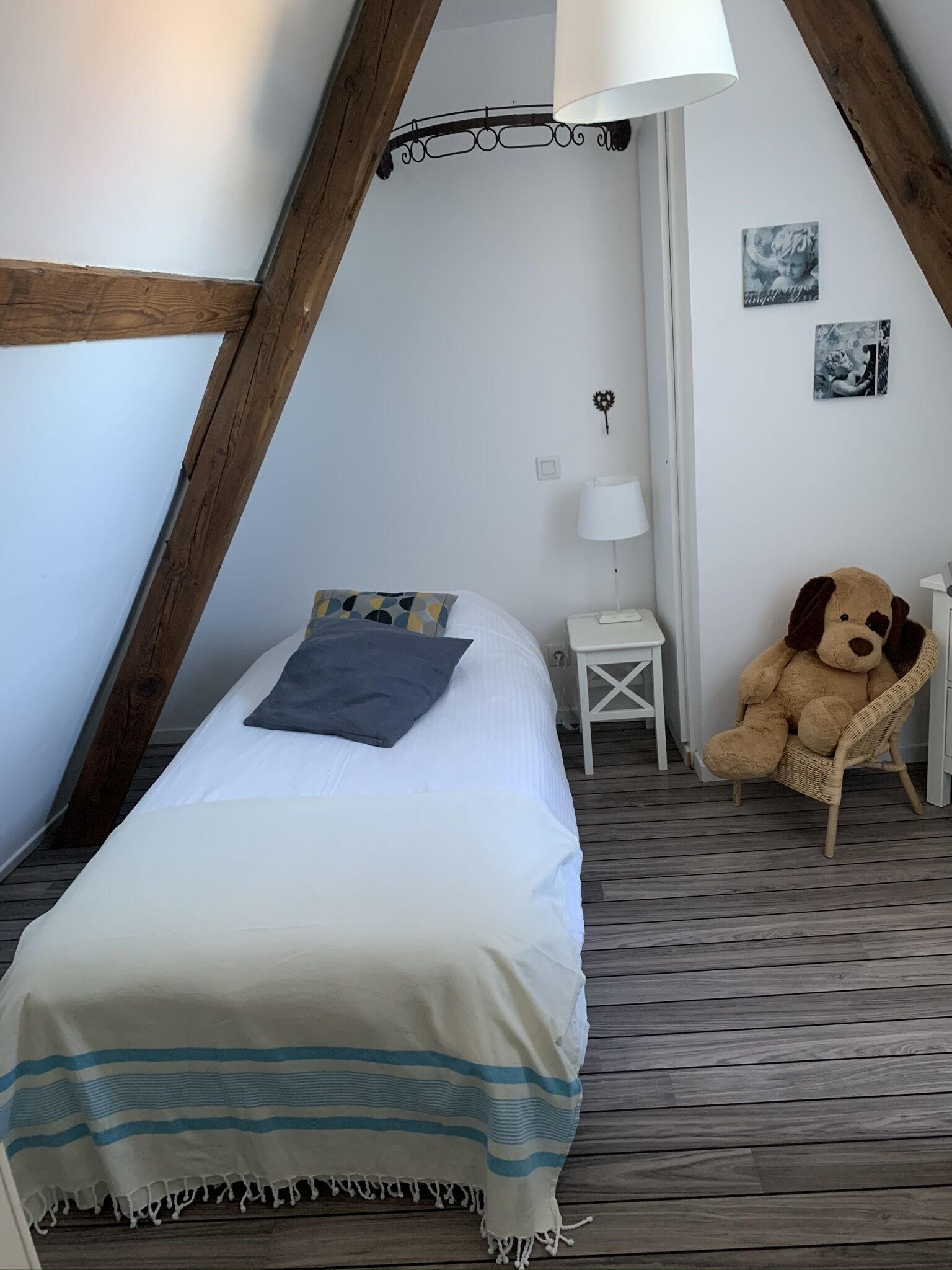 Een knus slaapkamer met een bed, een klein nachtkastje, een lamp, een teddybeer en een muur met foto’s.