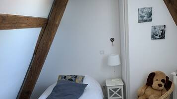 Een knus slaapkamer met een bed, een klein nachtkastje, een lamp, een teddybeer en een muur met foto’s.