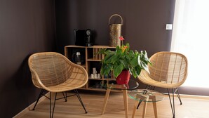 A modern living area with two wicker chairs, a glass coffee table, and a red pot with green plants. A wicker basket and a coffee machine are on a wooden shelf. - L'Ecurie d'Obernai (Obernai)