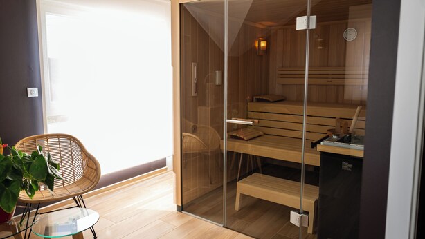 A modern room with a glass-walled sauna, wooden benches, and a glass table with a chair. - L'Ecurie d'Obernai (Obernai)