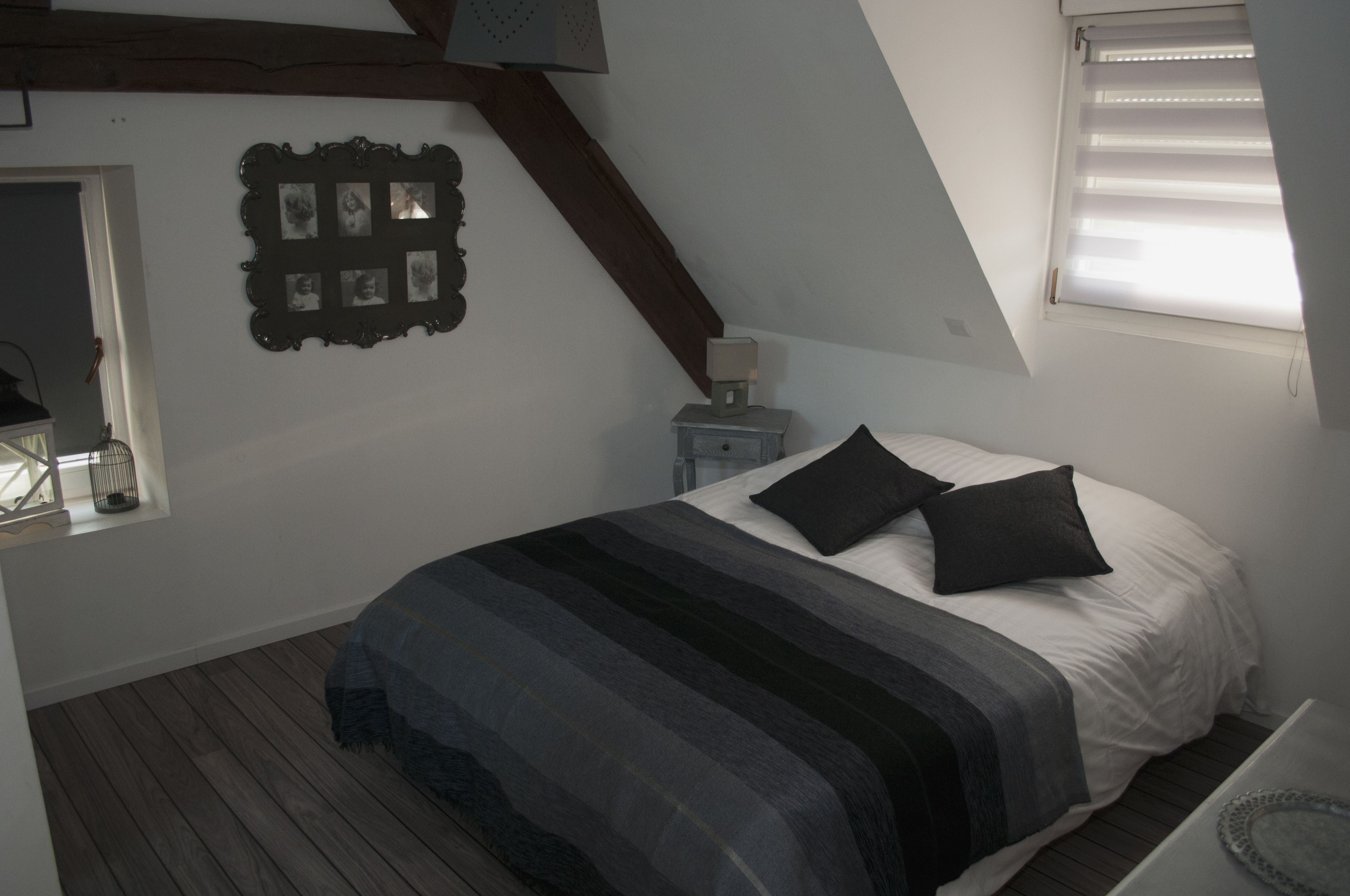 Une chambre à coucher avec un lit, une table de chevet, une lampe, un cadre photo et une fenêtre.