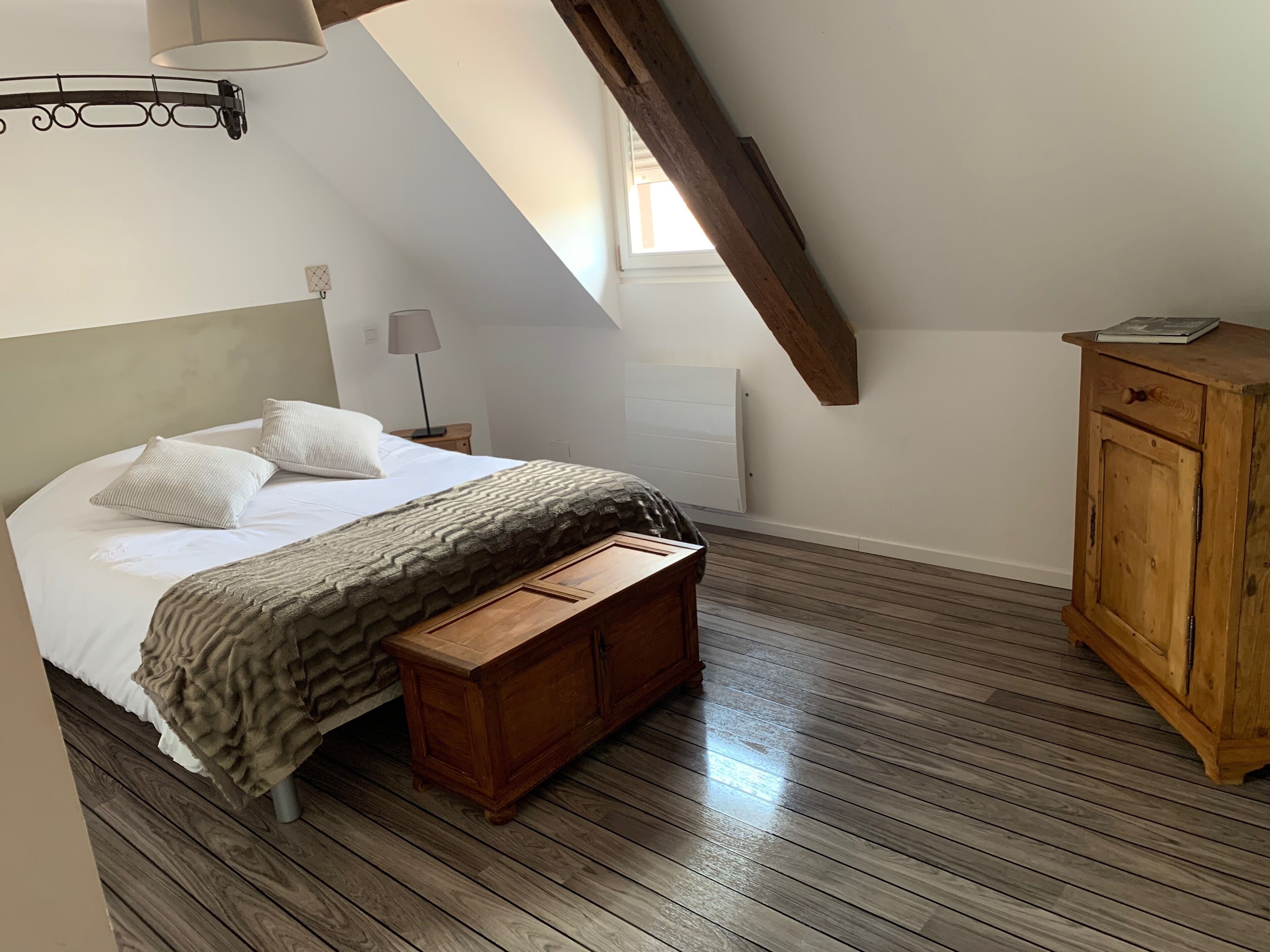A bedroom with a wooden bed, a bench, a wooden cabinet, a lamp, and a radiator.