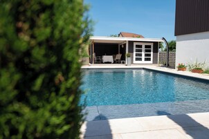 Una piscina con un porche techado, un muro de piedra y plantas en macetas.