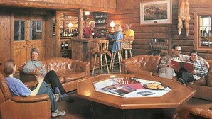 A rustic wooden interior with a bar area, leather seating, and a chess table. - Wood River Lodge (Nenana)
