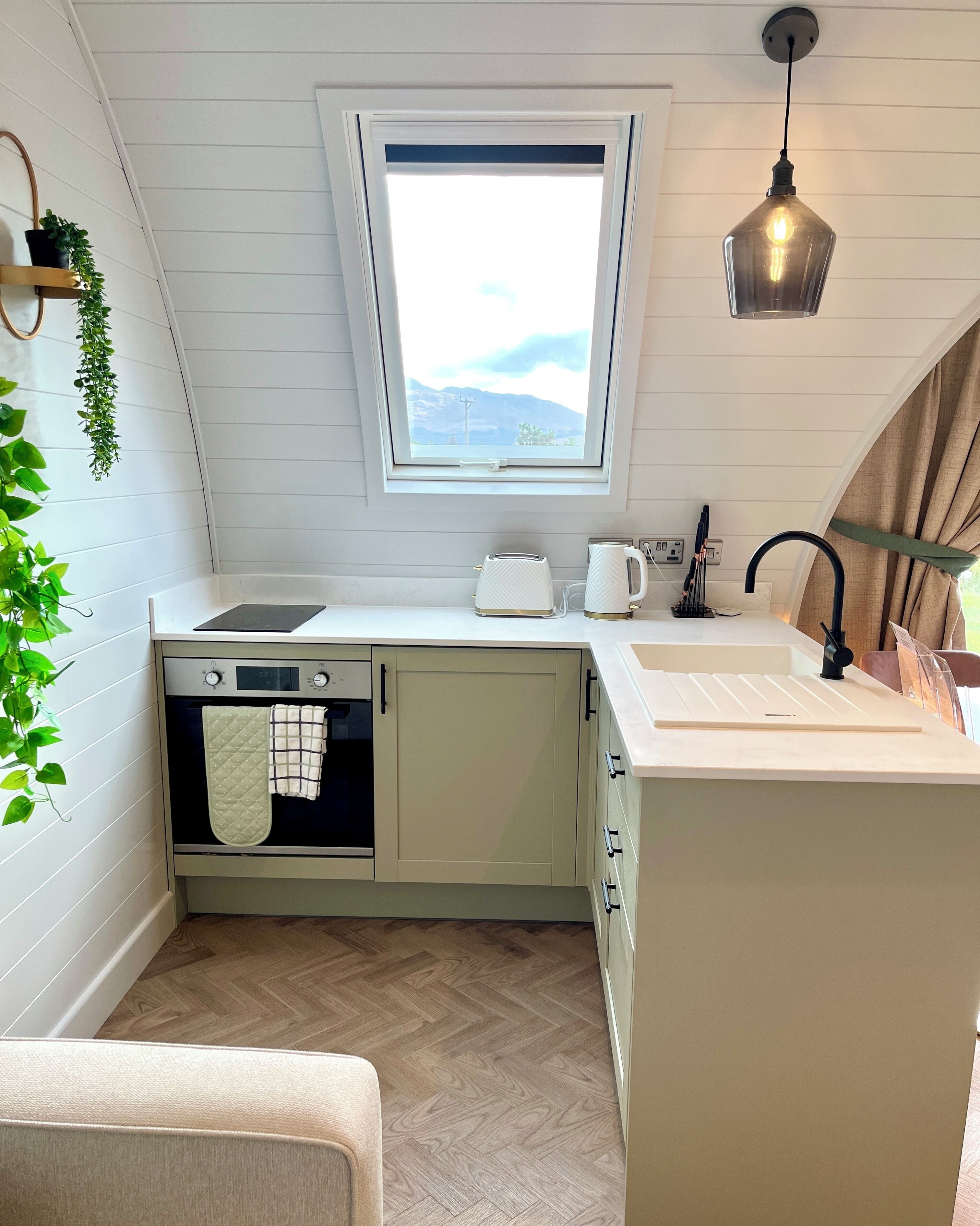 A compact kitchen with a built-in oven, a window with a view, a sink, and a kettle.