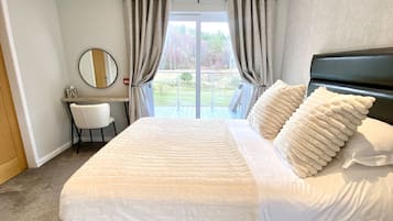 A bedroom with a large bed, a desk, a chair, a mirror, and a view of the outdoors.