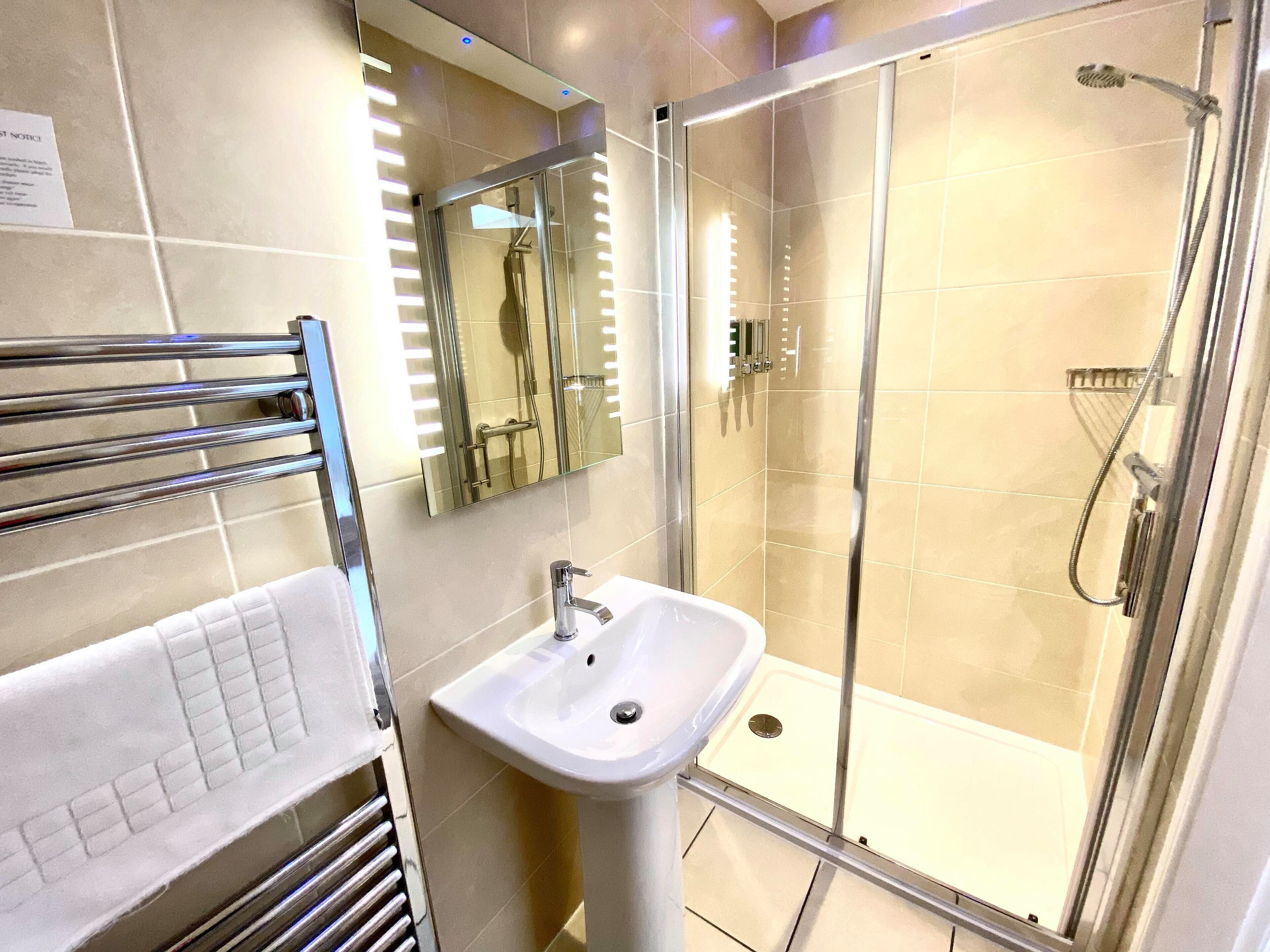 A modern bathroom with a glass-enclosed shower, a white sink, and a towel rack.