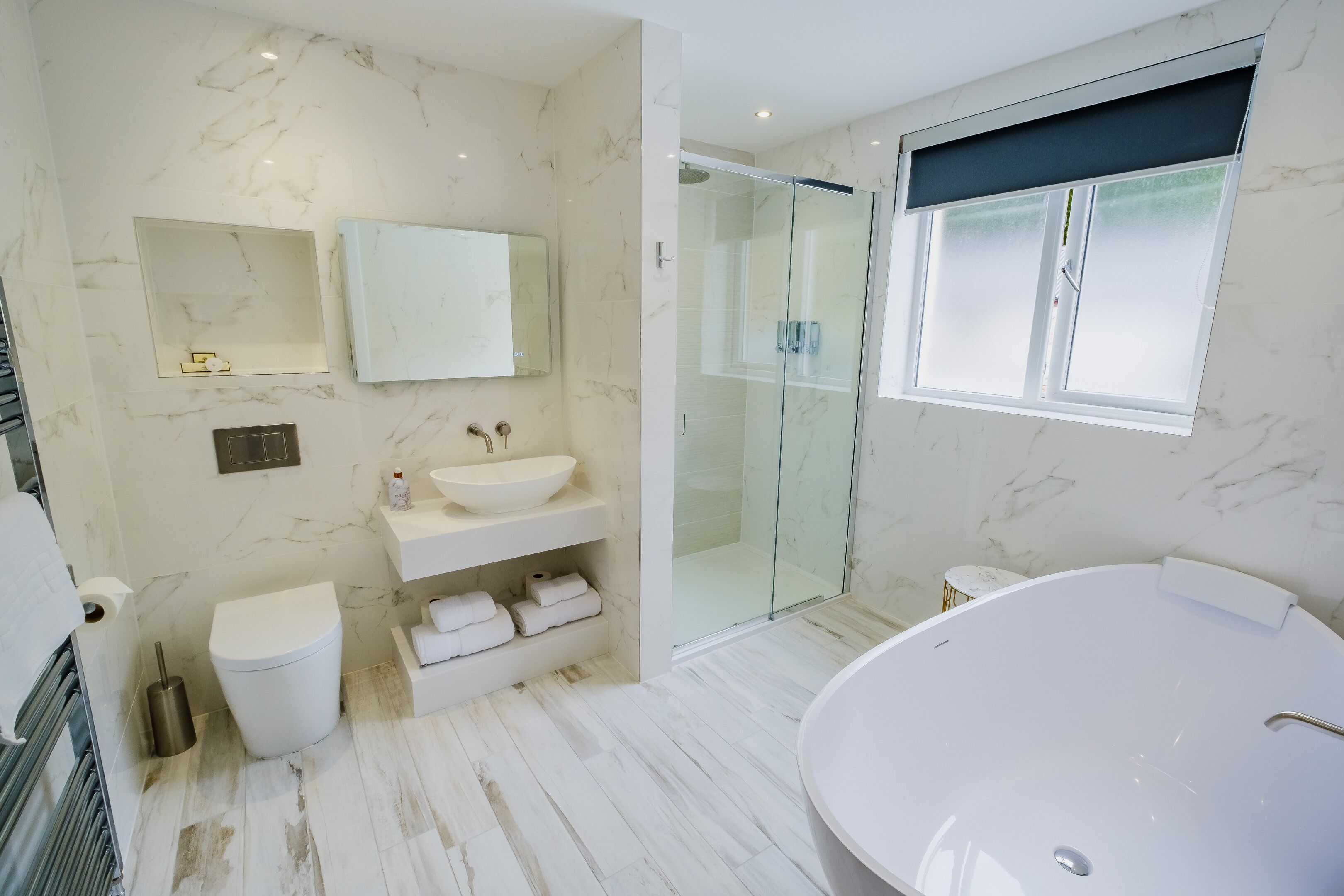 A modern bathroom with a large bathtub, a glass-enclosed shower, and a marble floor.