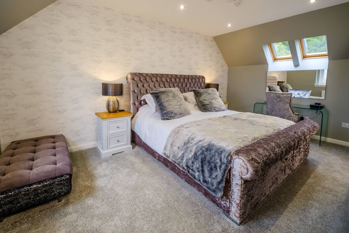 Ein Schlafzimmer mit einem großen Bett, einem Nachttisch, einem Sessel und einem Spiegel.