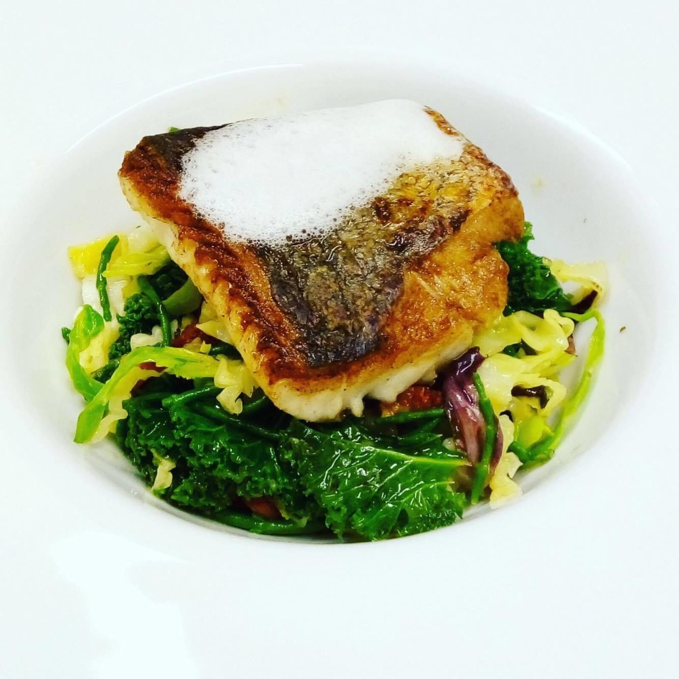 A dish with a piece of meat topped with a white sauce, served on a bed of greens.