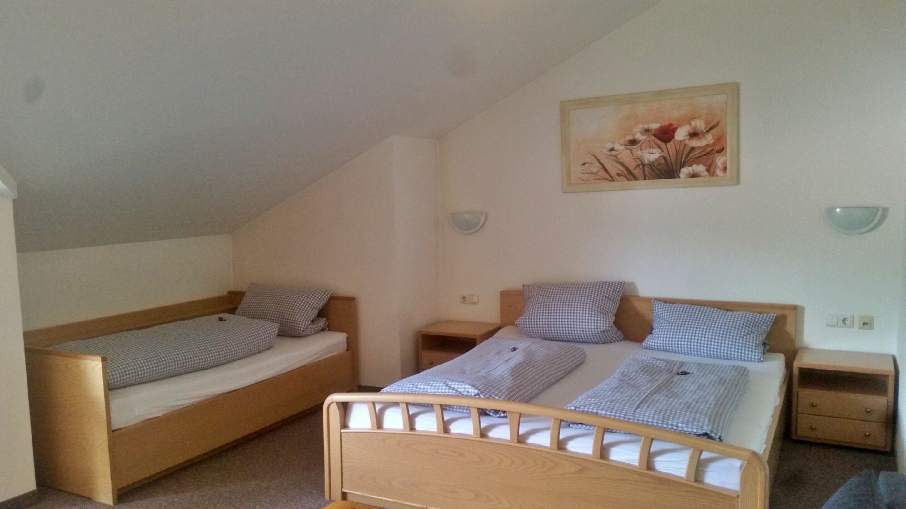 A small, simple room with two single beds, a nightstand, a wall-mounted light, and a painting.