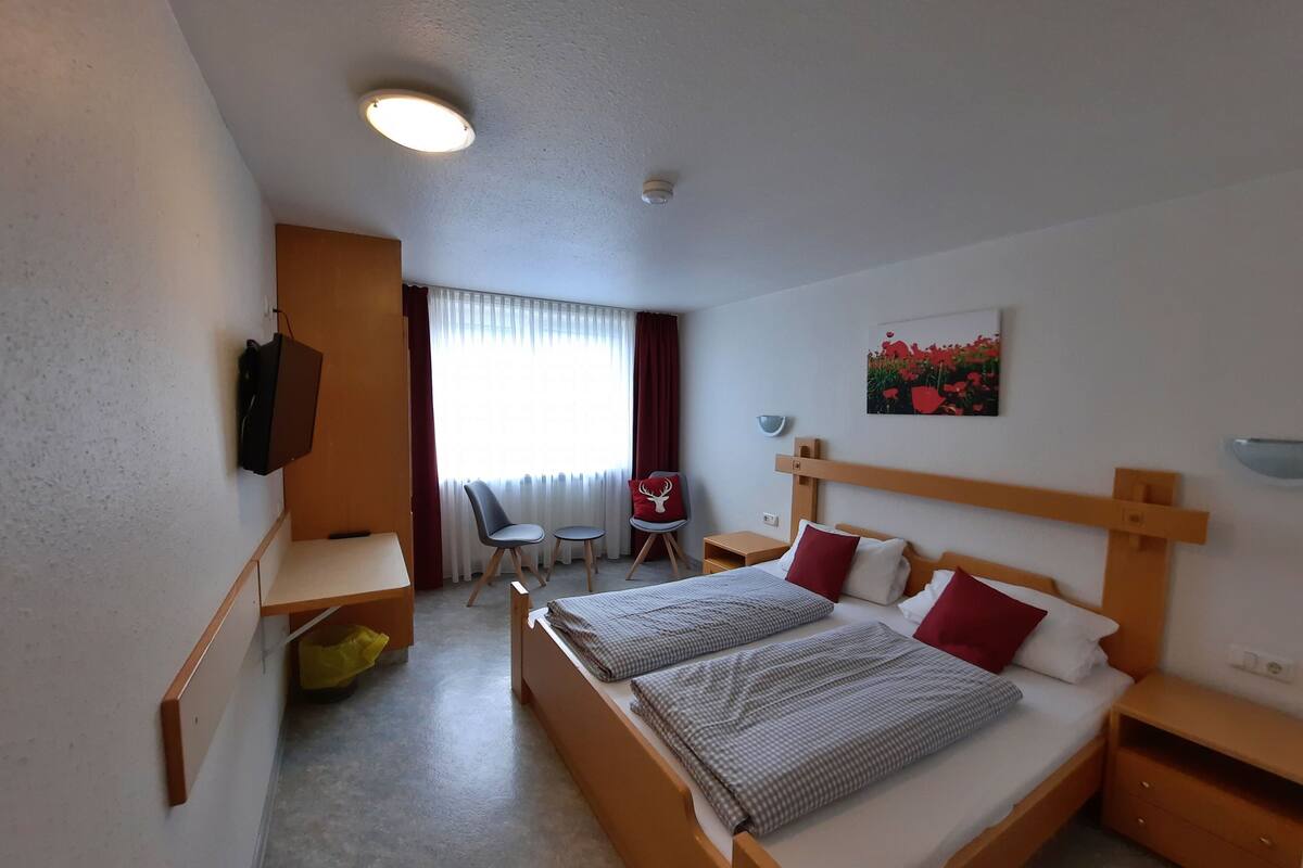 A hotel room with a bed, a desk, a chair, a TV, and a painting on the wall.