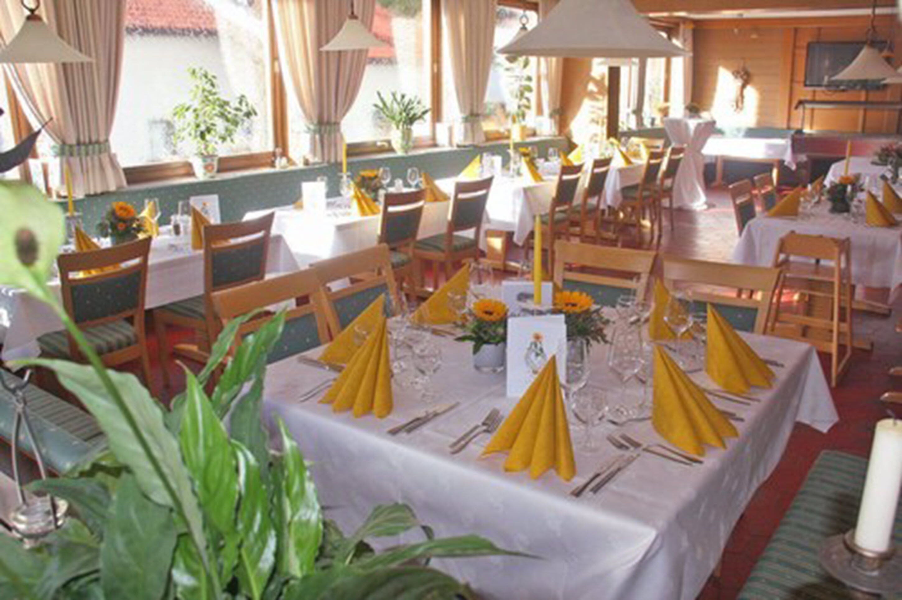 Un restaurante con varias mesas dispuestas, con servilletas amarillas, manteles blancos y velas.
