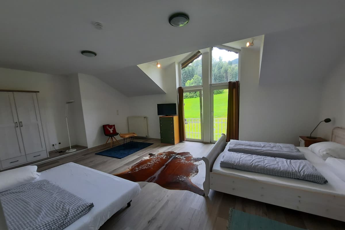 A modern bedroom with two beds, a wardrobe, a desk, and a view of a green landscape through a large window.