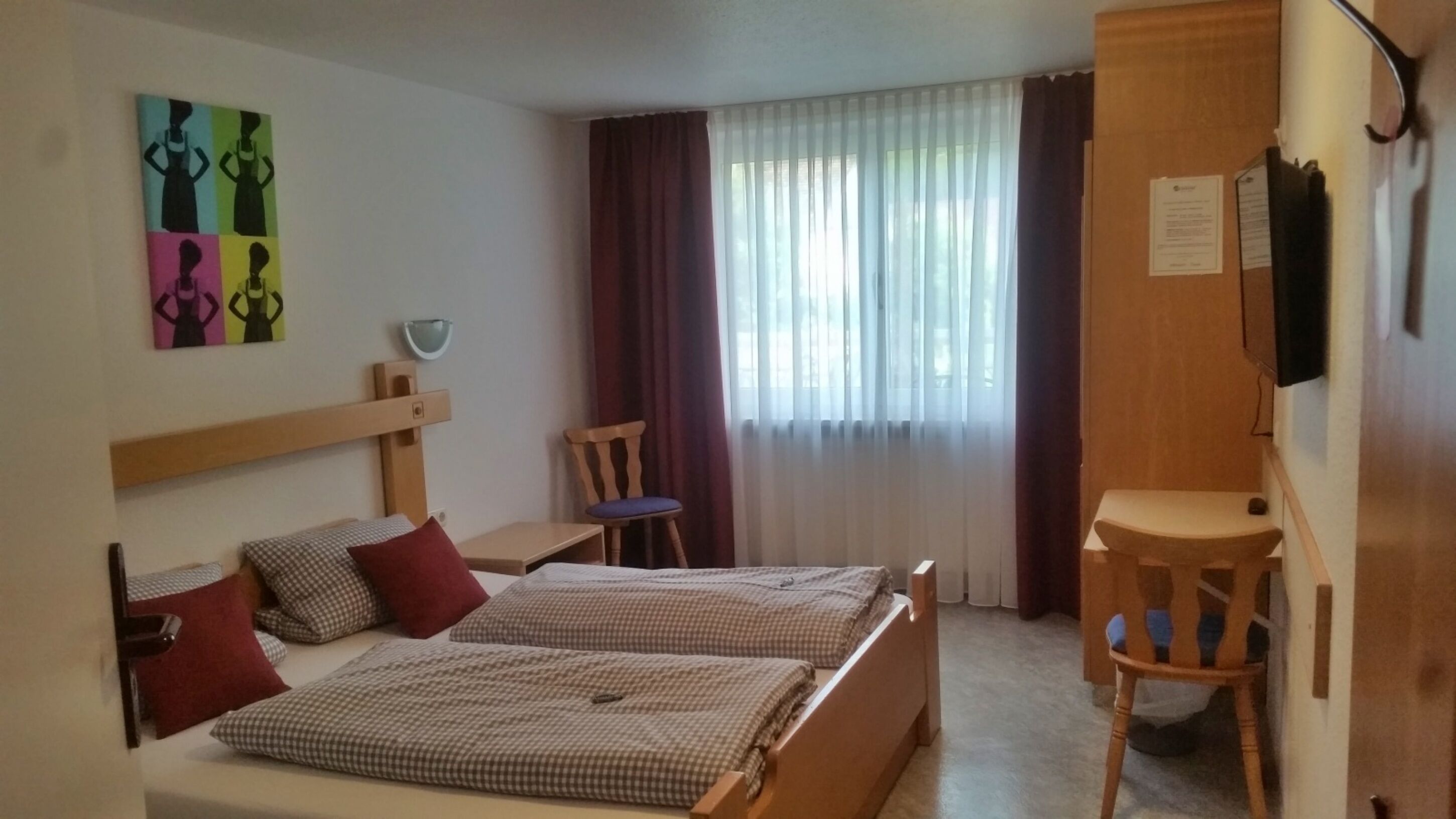 A hotel room with two beds, a desk, a chair, a TV, and a window with curtains.