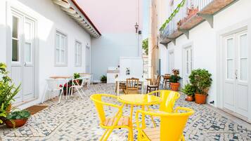 A courtyard with a tiled floor, white walls, and yellow chairs around a table.