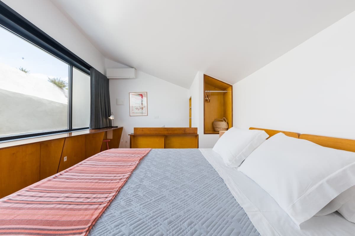 A modern hotel room with a large bed, a wooden headboard, a nightstand, and a window with a view of the outdoors.