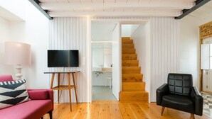 A modern living room with a wooden floor, a red sofa, a black leather chair, and a flat-screen TV on a stand. - Patio São Vicente Guest House (Lisbon)