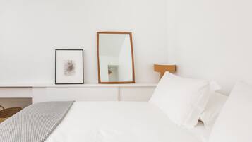 A neatly arranged bedroom with a bed, a framed picture, a mirror, and a bedside lamp.