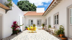 A courtyard with a tiled floor, a yellow table and chairs, potted plants, and a white building with a tiled roof. - Patio São Vicente Guest House (Lisbon)