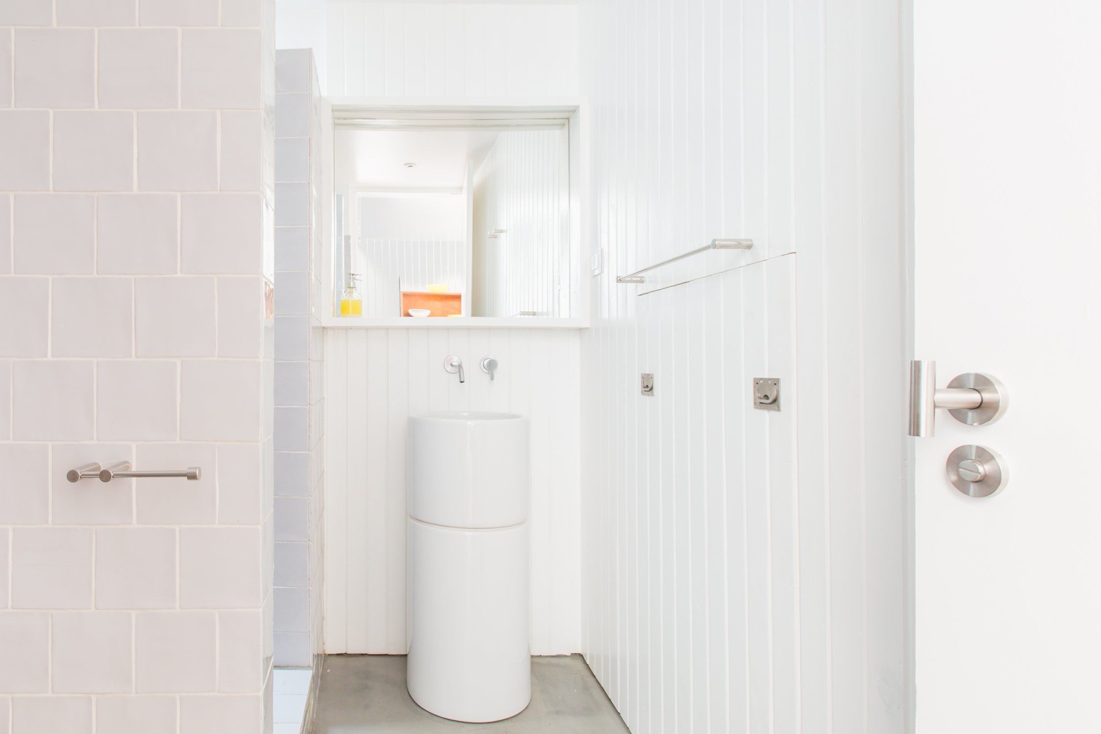 Een badkamer met witte betegelde wanden, een witte wastafel en een spiegel erboven.