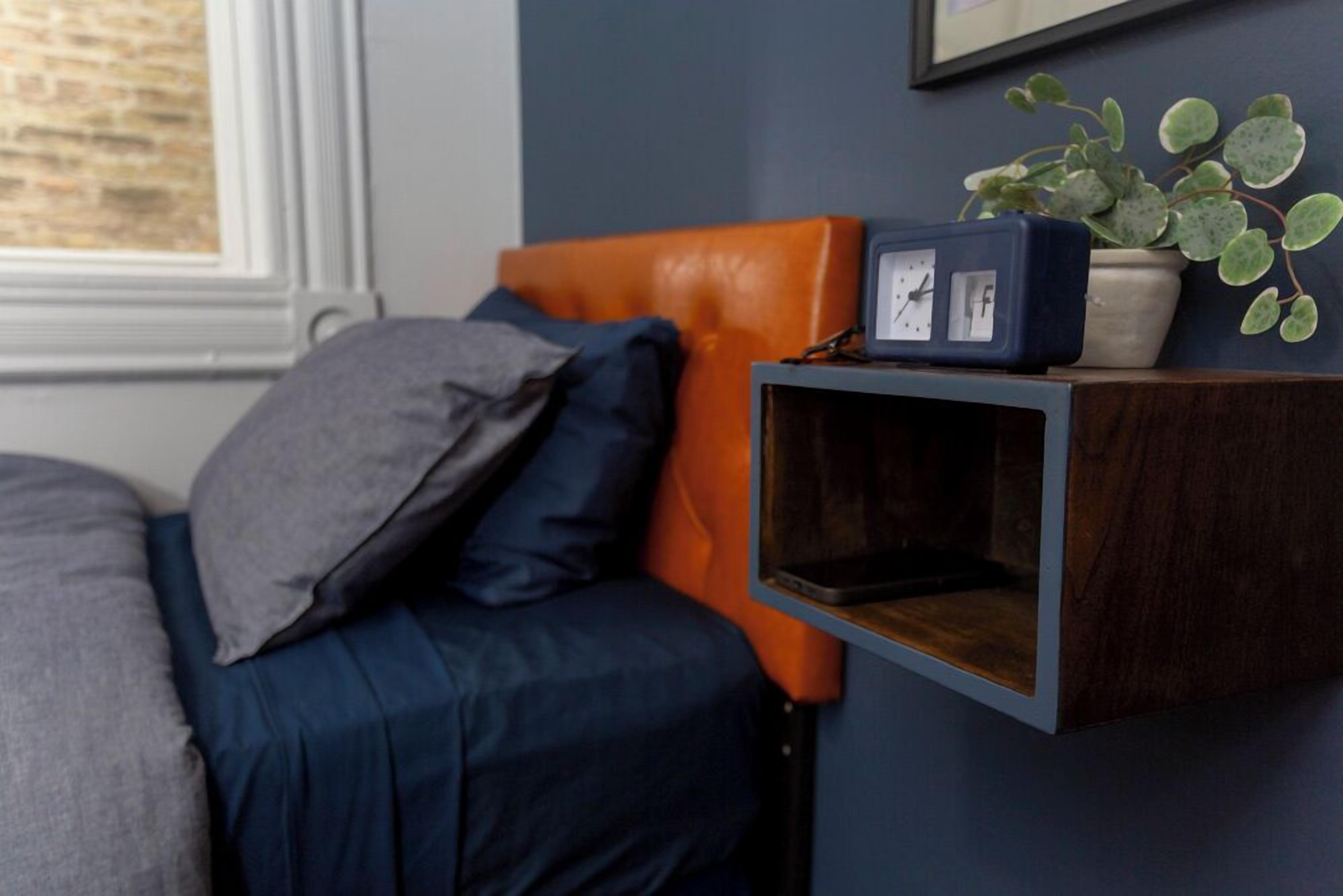 A bedroom with a bed, a nightstand, a clock, and a potted plant.