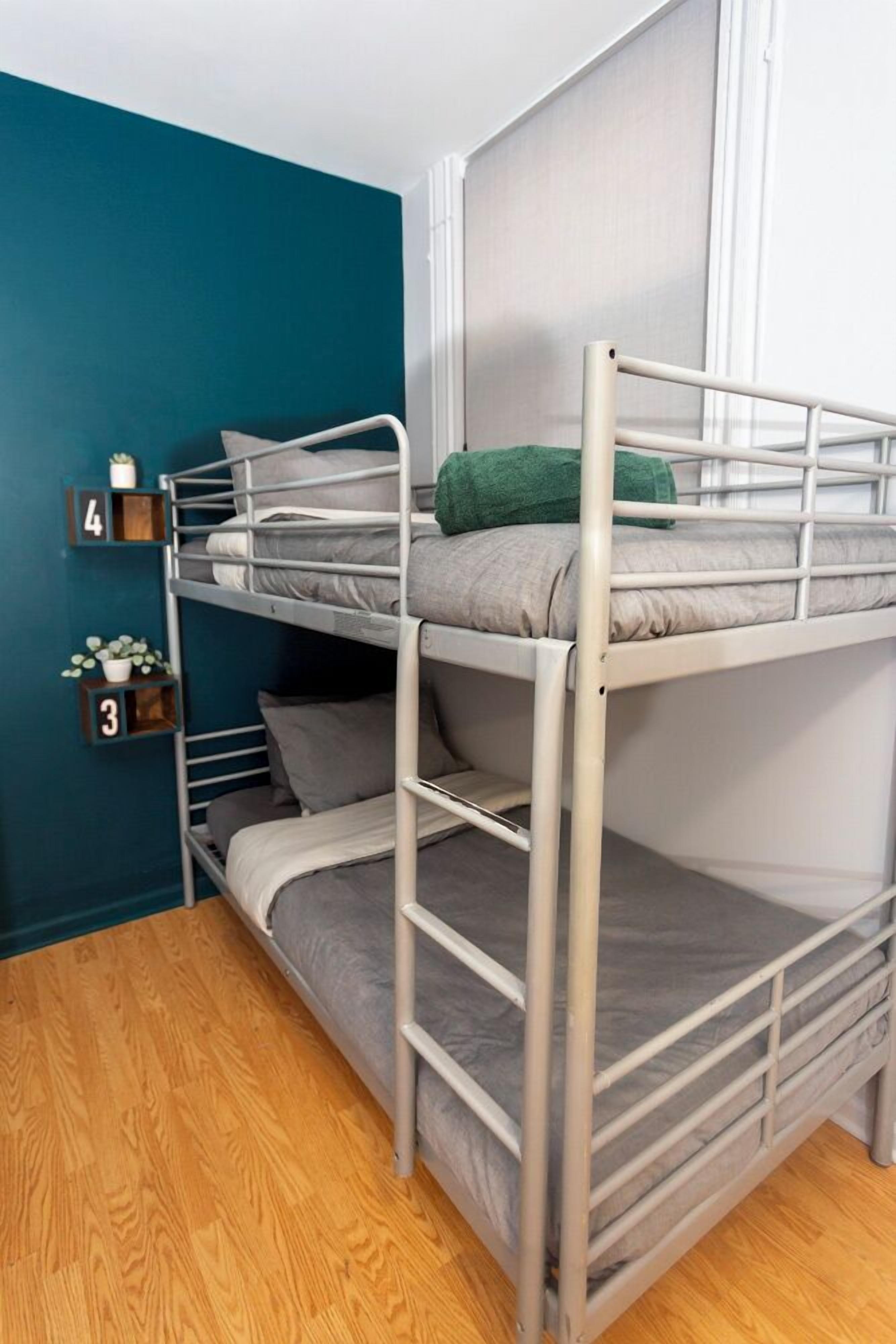 Een stapelbed met grijze beddengoed, een groen kussen en een turquoise accentmuur.