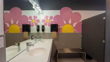 A modern bathroom with a large mirror, two sinks, a shower area, and a decorative wall with floral patterns.