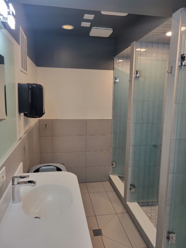 A modern bathroom with a large white sink, a glass shower enclosure, and a wall-mounted soap dispenser.